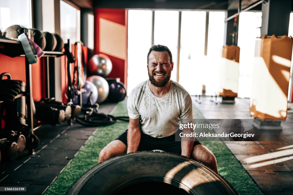 Männlicher Athlet zuckt vor Anstrengung während des Truck Tire Gym Workouts zusammen