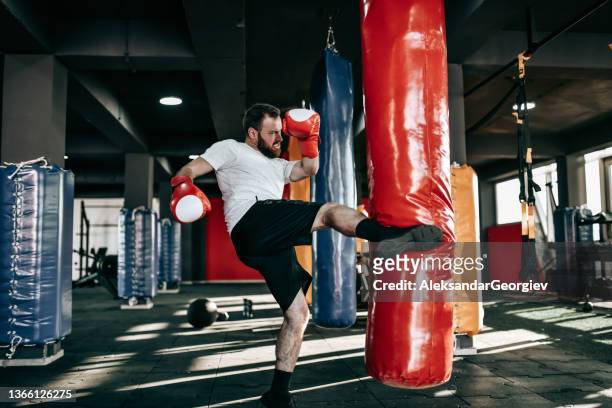 male kickboxer working on leg kicks with heavy bag - boxing bag stock pictures, royalty-free photos & images