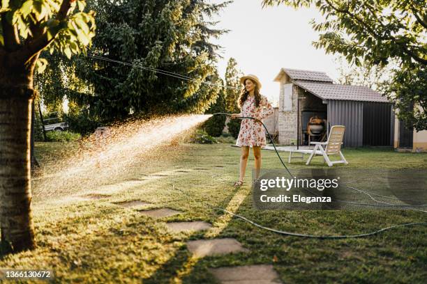 shot of a woman watering plants with a garden hose in backyard - water geven stockfoto's en -beelden