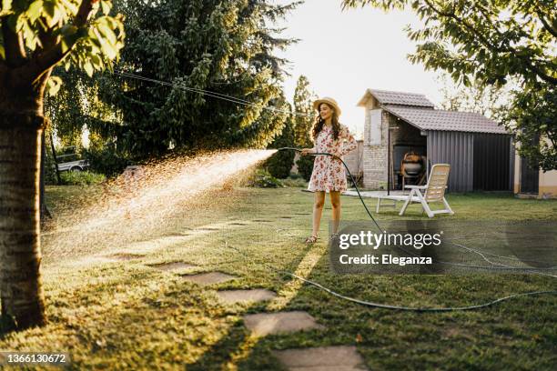 shot of a woman watering plants with a garden hose in backyard - garden of dreams foundation press conference stockfoto's en -beelden