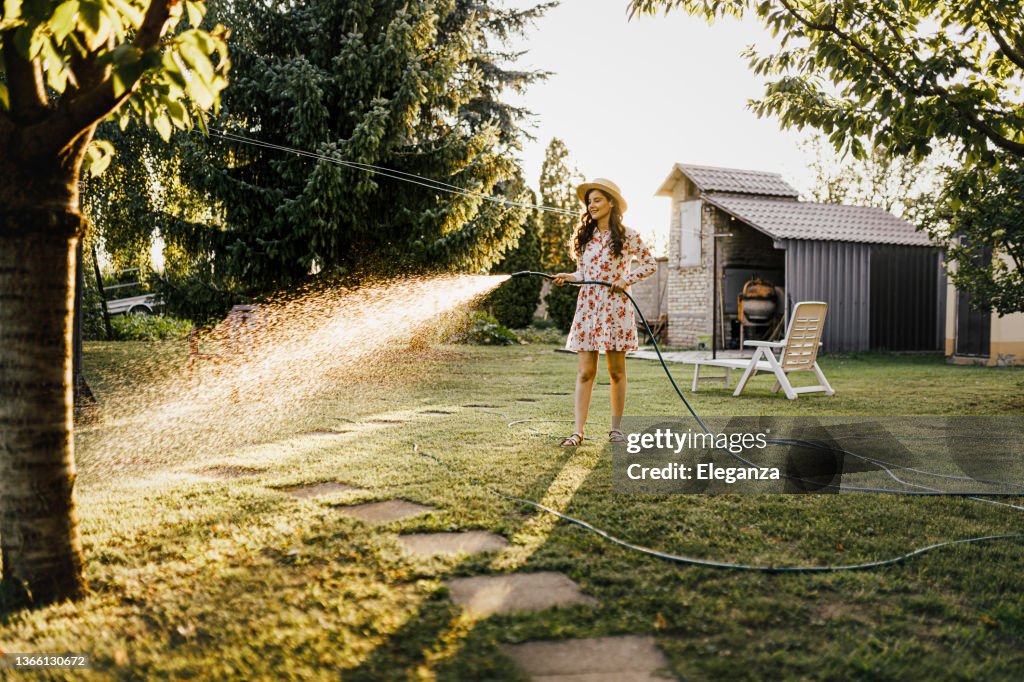 Shot of a woman watering plants with a garden hose in backyard