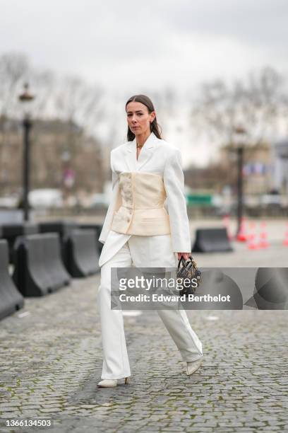 Alice Barbier wears a white oversized blazer jacket, a beige corset, matching suit pants, a Lady Dior bag, pointed shoes, outside Dior, during Paris...