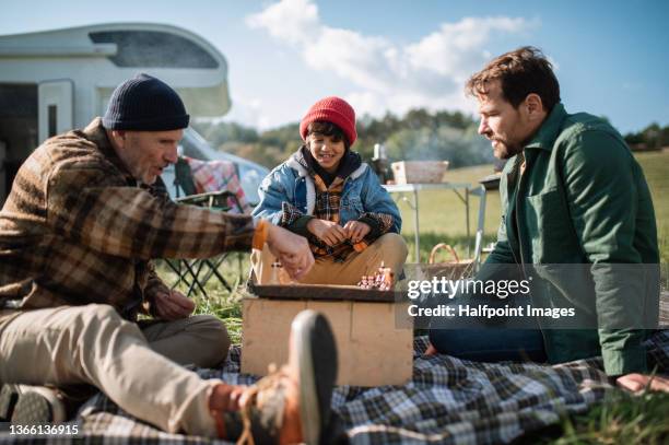 little boy camping with his father and grandfather in nature, playing chess together. - camping games stockfoto's en -beelden