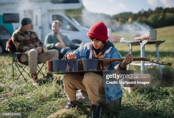 little multiracial boy sitting with guitar when camping with father and grandfather - motorhome winter stock-fotos und bilder