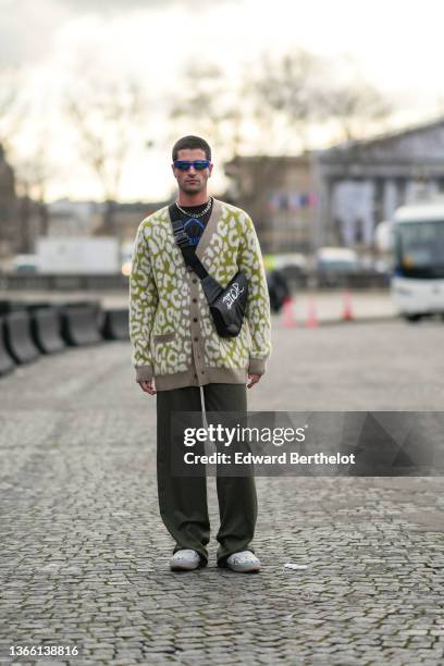 Marc Forne wears blue sunglasses, a necklace, a black and blue t-shirt, a green and white oversized wool cardigan, a Dior black leather Saddle bag...