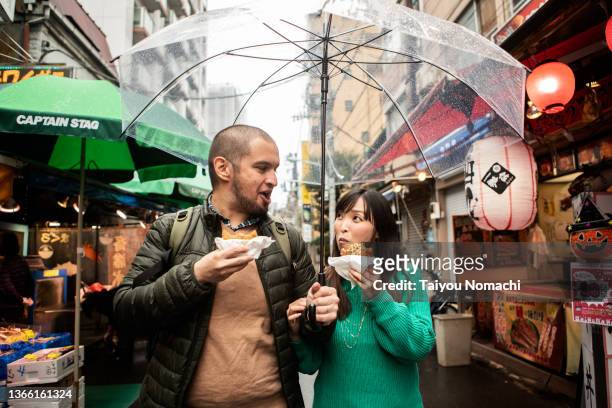 an internationally married couple who came to tsukiji for sightseeing while eating fried food - カップル　外国人 ストックフォトと画像