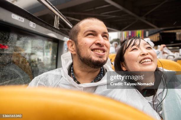 a couple enjoying a trip and sightseeing on an open-top bus despite the rain - open top bus stock pictures, royalty-free photos & images