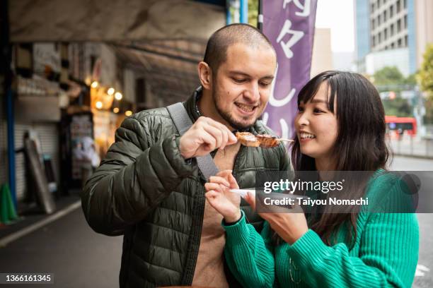 an internationally married couple who came for sightseeing eating fish at a food stall - tsukiji outer market stock pictures, royalty-free photos & images