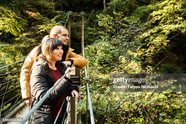 an internationally married couple gazing at the scenery from a suspension bridge - traveling internationally stock pictures, royalty-free photos & images