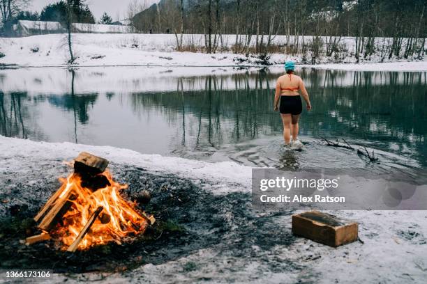 a women wades through the cold waters of a river surrounded by snow for a new years day polar bear swim - bear camping stock pictures, royalty-free photos & images