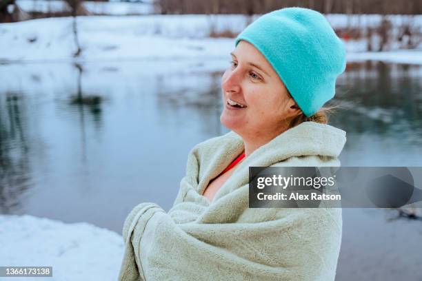 a women laughs while wrapped in a towel after swimming in a river surrounded with snow - nieuwjaarsduik stockfoto's en -beelden