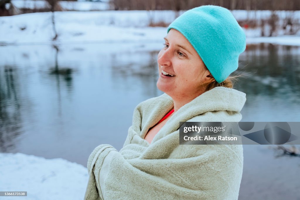A women laughs while wrapped in a towel after swimming in a river surrounded with snow