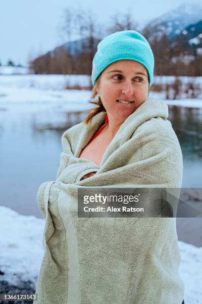 a women makes a funny face while wrapped in a towel after swimming in a river surrounded with snow - nieuwjaarsduik stockfoto's en -beelden