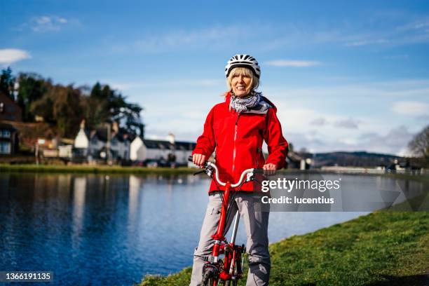 senior woman cycling the caledonian canal at inverness, scotland - cycling helmet stock pictures, royalty-free photos & images