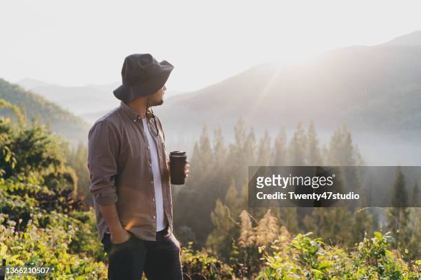rearview of a man standing on the mountain holding a coffee cup enjoys summer camping - japanese tents stock pictures, royalty-free photos & images