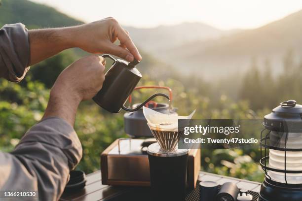 rearview of a man making dripping coffee on the picnic table while camping on th mountain in morning - brewed coffee stock-fotos und bilder