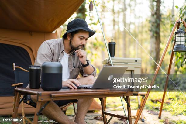 man enjoys camping sitting in front the camping tent using laptop working remotely - time off work stock pictures, royalty-free photos & images