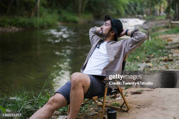 man enjoys summer camp drinking coffee beside the river in forest - foldable stockfoto's en -beelden
