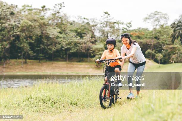 mother teaching son to ride a bicycle - indonesia family stock pictures, royalty-free photos & images