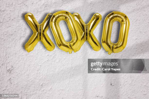 xoxo single word in golden foil balloon against brick white surface wall - happy anniversary stock-fotos und bilder