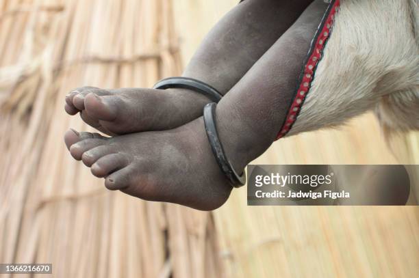 a baby's feet are seen as the baby is carried by a mother in a goatskin bag under her arm in south sudan. - sudan del sur fotografías e imágenes de stock