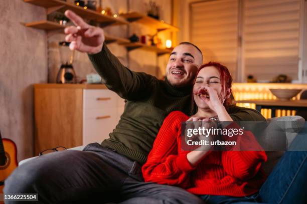 young couple watching tv on the sofa - the love life and reality show stock pictures, royalty-free photos & images