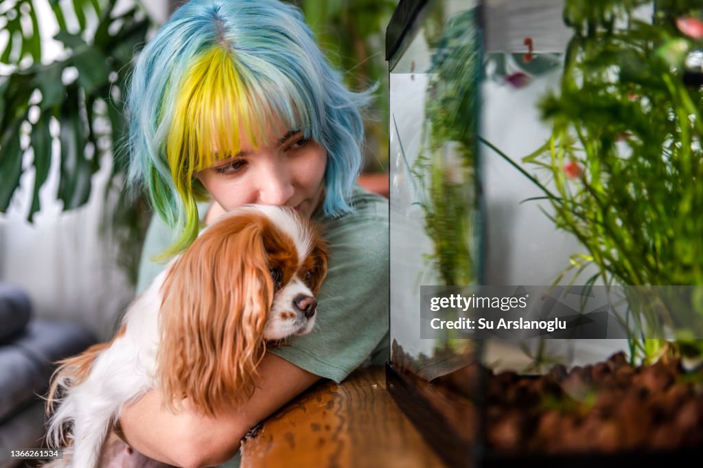 Young girl with colored hair looking at the fishbowl with her dog