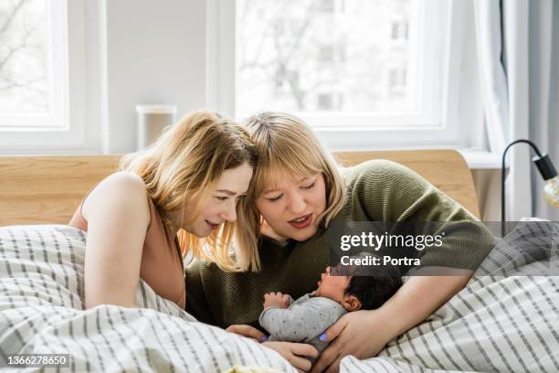 lesbian couple with their baby boy lying in bed - gay couple stock pictures, royalty-free photos & images