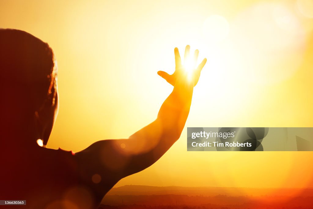 Young woman reaching for the sun.