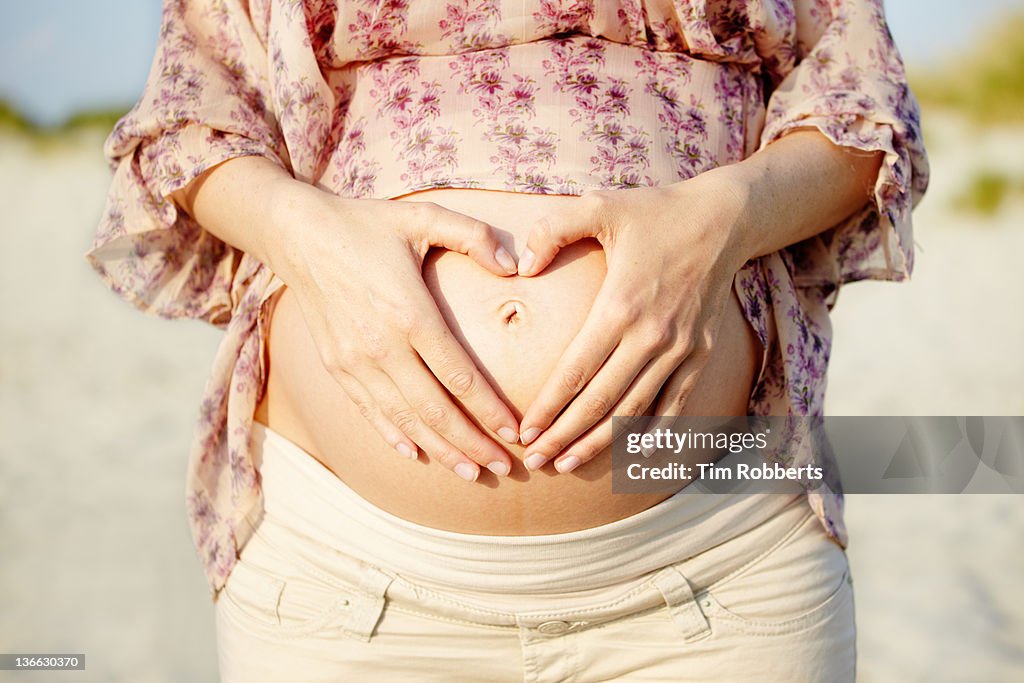 Pregnant woman making heart shape on her bump.