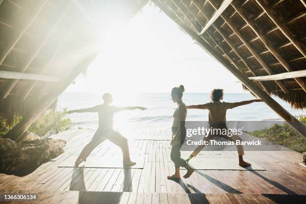 wide shot of gay couple taking sunrise yoga class in beachfront pavilion at luxury tropical resort - pavilion stock pictures, royalty-free photos & images