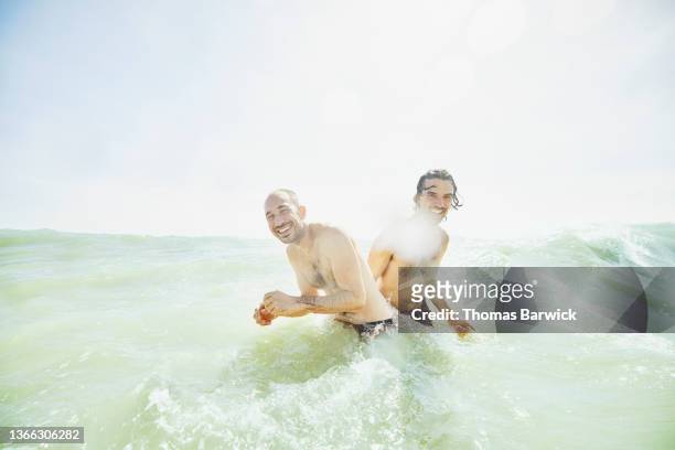Wide shot of smiling and laughing gay couple playing in surf at tropical beach