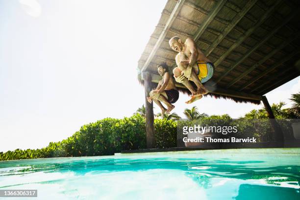 wide shot of gay couple jumping into pool at luxury tropical villa while on vacation - resort enjoy ストックフォトと画像