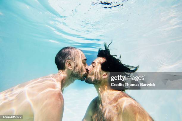 medium wide underwater shot of gay couple kissing underwater in pool while on vacation - gay kiss stock pictures, royalty-free photos & images