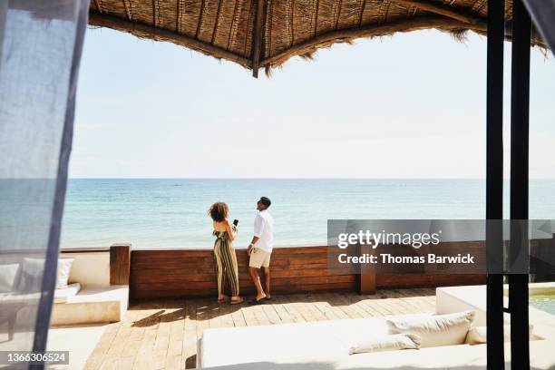 wide shot of smiling couple enjoying view of ocean from deck of luxury tropical villa - suite photos et images de collection