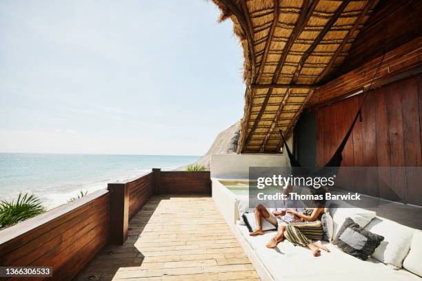 wide shot of couple relaxing on deck of luxury tropical villa overlooking ocean - luxury hotel fotografías e imágenes de stock