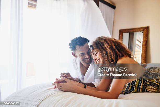 medium wide shot of smiling couple relaxing on bed in luxury suite at tropical resort - couple in bed fotografías e imágenes de stock