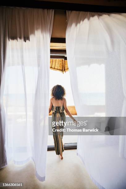 Wide shot of woman walking through curtains to deck of luxury tropical villa