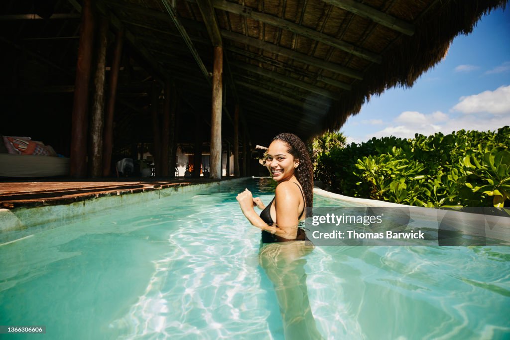 Wide shot of smiling woman relaxing in pool at luxury tropical villa
