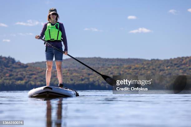 woman paddleboarding on the lake in autumn, quebec, canada - life jacket stock pictures, royalty-free photos & images