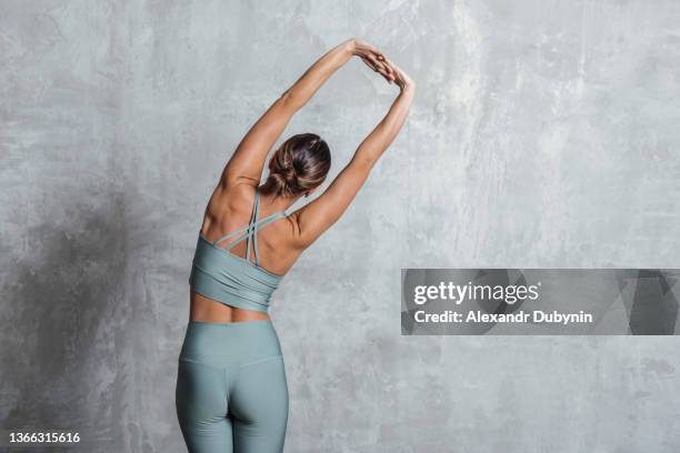 woman doing back stretch practicing yoga standing against wall background with copy space. - performance concept stock pictures, royalty-free photos & images