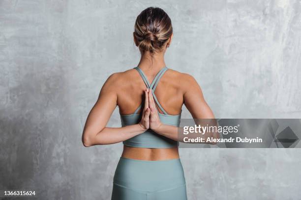back of woman practicing yoga standing portrait on gray wall. sport and healthy lifestyle concept - back stretch stock pictures, royalty-free photos & images