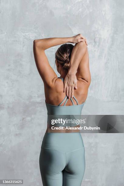 back view woman doing yoga workout portrait on gray wall. sport and health concept - man touching shoulder stock-fotos und bilder