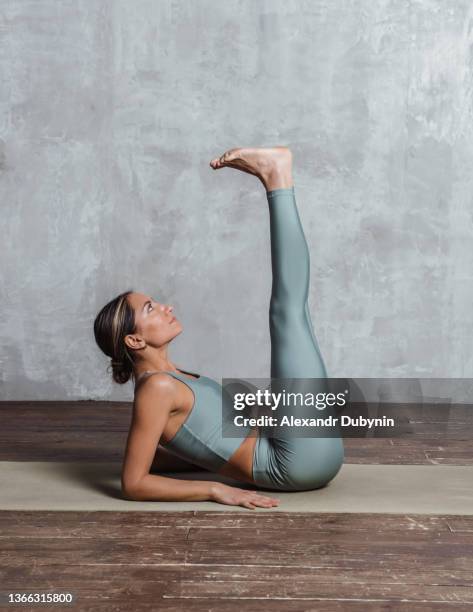 slim athletic woman practicing yoga lying on mat on the floor doing leg up exercise on abs muscles. sport and healthy body concepts - dorsal fin stock photos et images de collection