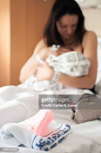 close up of a pink wooly hat on top of a towel and a mother lying down on a bed holding her newborn baby girl wrapped up in a blanket on the background in a flat in edinburgh, scotland, uk - girls in bras photos stock pictures, royalty-free photos & images