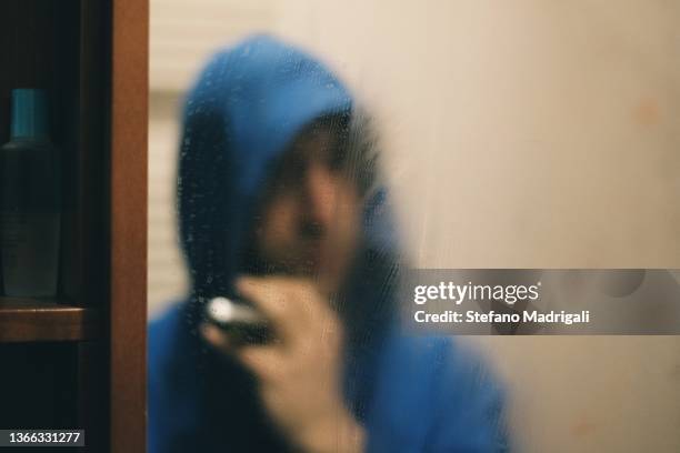 man shaving his beard in the mirror with electric razor - mirror steam stockfoto's en -beelden