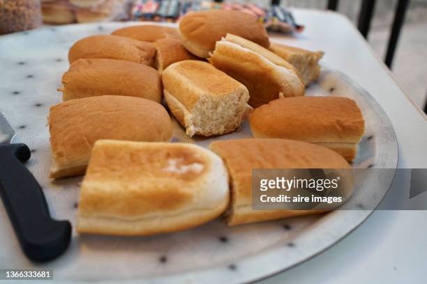 close up of golden hot dog buns cut in half on a plate resting on a table with white tablecloth. - cut in half ストックフォトと画像