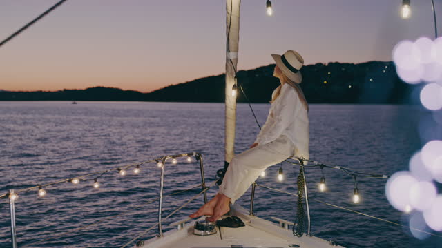 SLO MO Trendy woman enjoys the view from a deck of a sailboat illuminated with string lights
