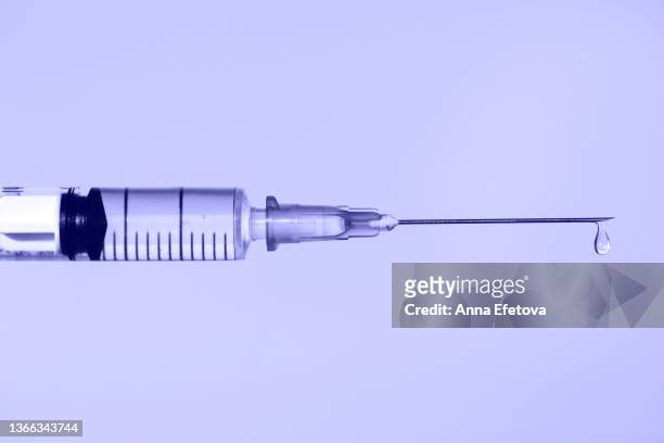 disposable sterile syringe with drop of fluid medication on thin needle on violet background. macro photography with copy space. demonstrating very peri - color of 2022 year - syringe stock-fotos und bilder