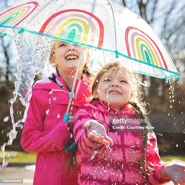 schwestern im grundschulalter gehen mit dem vater spazieren und spielen im regen mit regenschirmen - girl smiling on rain stock-fotos und bilder